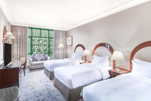 a hotel room with three beds and a television at Madinah Hilton Hotel in Al Madinah