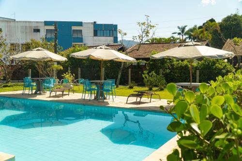 una piscina con mesas, sillas y sombrillas en Pousada Dunasol Floripa, en Florianópolis