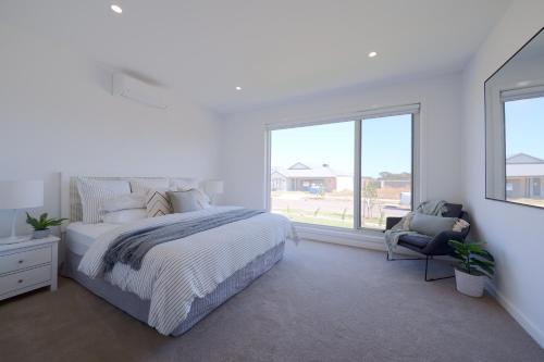 a white bedroom with a large bed and a chair at Modern Spacious Coastal Villa in Ocean Grove