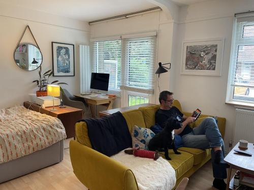 a man sitting on a couch reading a book with a dog at Charming studio Apartment in London in London