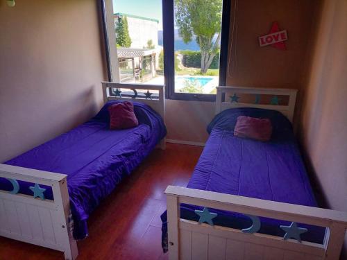 two beds in a room with purple sheets and a window at hermosa casa a una cuadra del lago in San Carlos de Bariloche