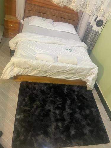 uma cama com lençóis brancos e um tapete preto no chão em The first royal tour lodge em Dodoma