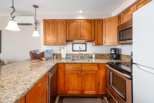 a kitchen with wooden cabinets and granite counter tops at Maalaea Kai 311 - Direct Ocean Front, Split AC in Wailuku