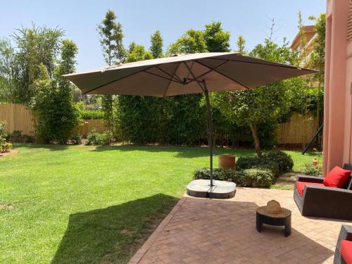 a patio with an umbrella and a couch and a chair at Villa rouge avec piscine et golf in Marrakech