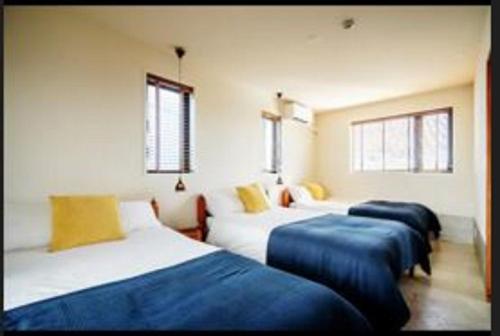 um quarto com três camas com lençóis azuis e janelas em senahahausub03 em Yomitan