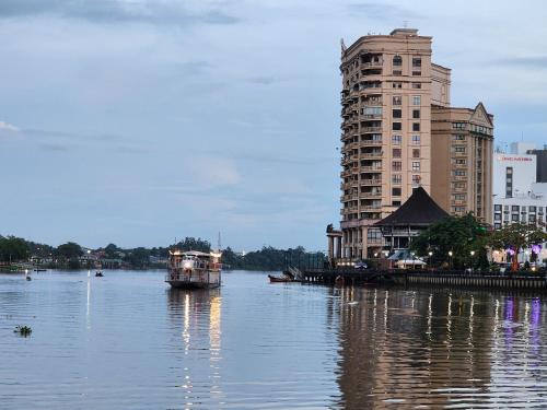 a boat on a river next to a tall building at Riverbank Suites Kuching Waterfront in Kuching