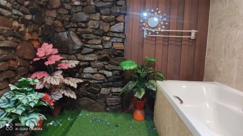 baño con pared de piedra, bañera y plantas en Villa Dalam Laut 580, en Pantai Cenang