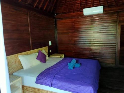Cama en habitación de madera con sábanas y almohadas moradas en Bunutbali Villas88, en Nusa Lembongan