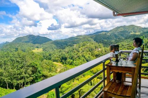 a woman sitting at a table on a balcony with a view of mountains at BANAUE EVERGREEN HOSTEL AND RESTAURANT in Banaue