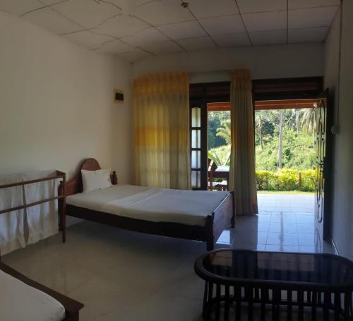 a bedroom with a bed and a table and a window at Rainforest River Edge in Deniyaya