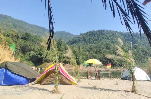a group of tents on a beach with mountains in the background at Dawki, Frankenstein adventure camp, riverside camping in Dawki