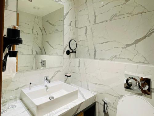 a white bathroom with a sink and a mirror at Regenta - The World Surat in Surat