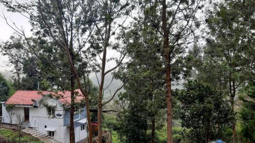 a white house with a red roof and some trees at jacaranda resorts in Kanthalloor