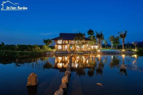 una casa grande en el agua por la noche en Bavi Annam Garden, en Ba Vì