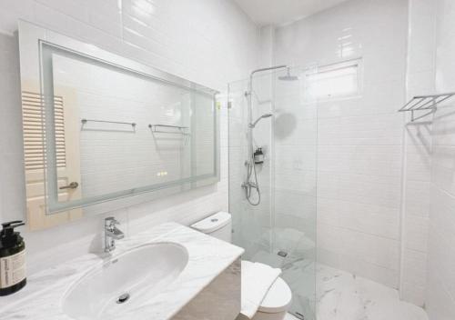 een witte badkamer met een wastafel en een douche bij Baan Naya ที่พักสัตหีบ in Ban Chang