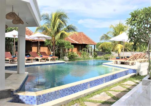 a swimming pool in a resort with tables and umbrellas at Green Village Jungle Resort in Nusa Penida