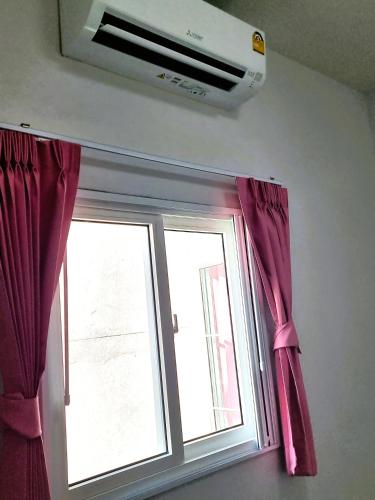 a window with pink curtains and a air conditioner at Airport Neko House in Hat Yai
