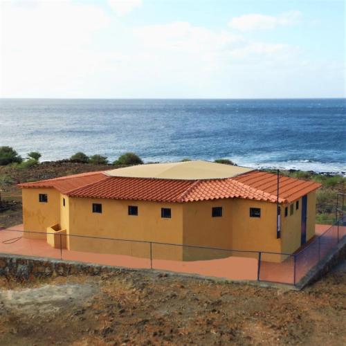 uma casa amarela com um telhado vermelho ao lado do oceano em Casa Tartaruge + Casa Pardal em Carriçal