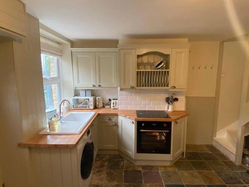 a kitchen with white cabinets and a sink and a dishwasher at Cosy two bed townhouse in Centre of C.Norton in Chipping Norton