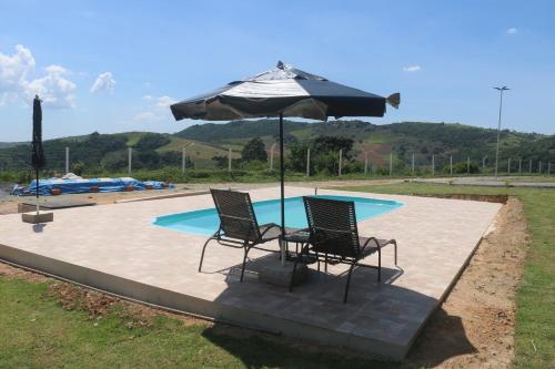 zwei Stühle und ein Sonnenschirm vor einem Pool in der Unterkunft Sítio Terra Sertaneja - Chalé Um Sonhador in Piedade