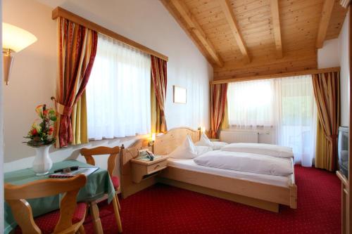 a hotel room with a bed and a desk and windows at Alpenhotel Landhaus Küchl in Kirchberg in Tirol