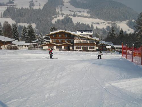two people skiing in the snow in front of a lodge at Alpenhotel Landhaus Küchl in Kirchberg in Tirol