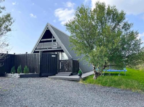 una pequeña casa con un árbol y un banco en Cabin in Lava Village with hot tub, en Selfoss