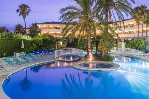 uma piscina de resort com palmeiras e cadeiras e um edifício em Mas Gallau em Cambrils