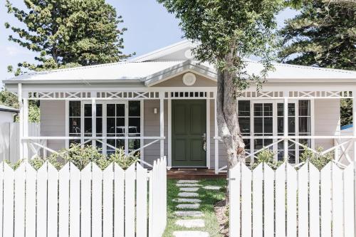 a white picket fence in front of a house with a green door at Bay Cottage in Patonga