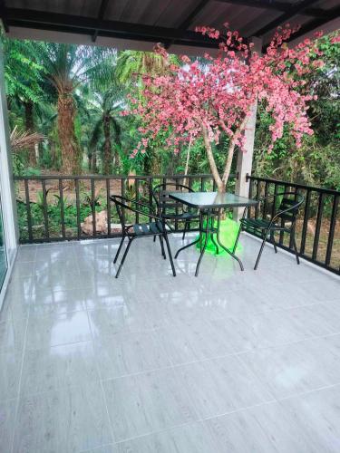 a patio with a table and chairs and a tree with pink flowers at Baan Namthip Homestay Trang บ้านน้าทิพย์ โฮมสเตย์ตรัง in Ban Huai To (1)