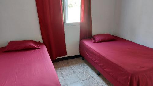 two beds in a room with red sheets and a window at Casa de descanso Grace in San José de Guatemala