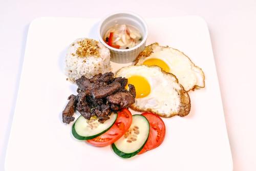 a plate of food with eggs meat and tomatoes at Ardenhills Suites in Manila