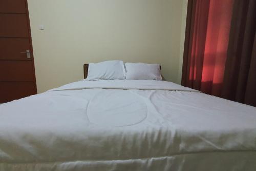 a white bed in a bedroom with a red curtain at Hotel O Wisma Haji BunbunNearYani Heahlerr in Rantau