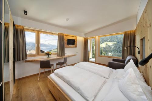 um quarto de hotel com uma cama, uma secretária e janelas em Hotel Sonne em Stelvio