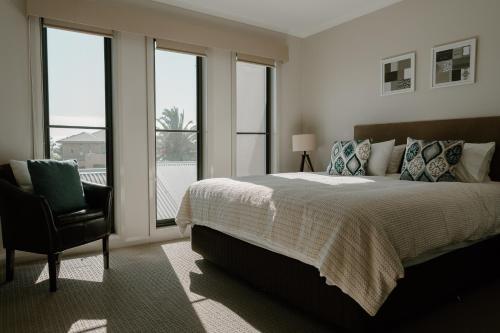 a bedroom with a bed and a chair and windows at Yarrawonga Waterfront Apartments in Mulwala