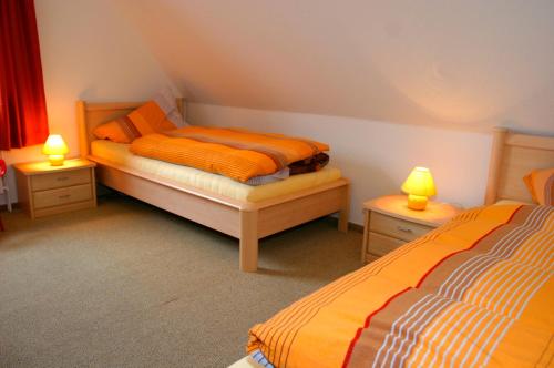 a bedroom with two beds with orange sheets and lamps at Rote Koje in Dagebüll