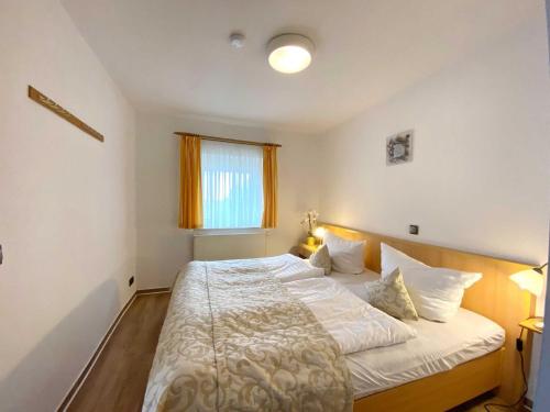 a bedroom with a bed with white sheets and a window at Süderhaus Hiddensee App 2 in Neuendorf