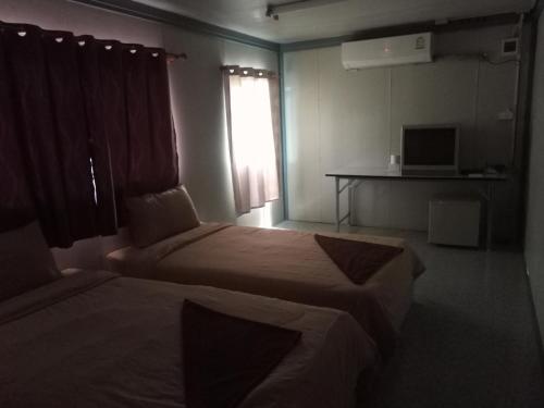 a room with two beds and a desk and a window at ปวินท์เกสต์เฮาส์ in Ban Pong Khlum