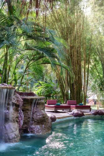 a pool with benches and a waterfall in a resort at The Namkhan, a Small Luxury Hotel of the World in Luang Prabang