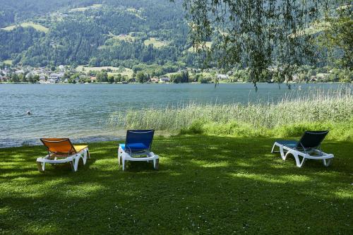 three chairs sitting in the grass next to a lake at FAST Ossiach in Ossiach