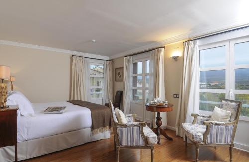 a bedroom with a bed and chairs and windows at Casona del Boticario in San Vicente de la Sonsierra