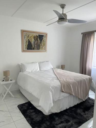a white bedroom with a bed and a ceiling fan at Luxury 1 Bdr Garden Cottage in Windhoek
