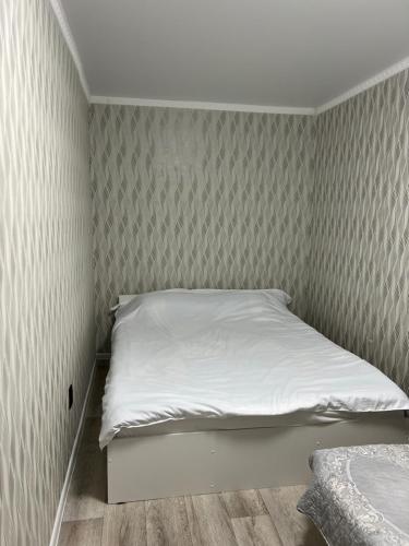 Cette petite chambre comprend un lit avec des draps blancs. dans l'établissement Апартаменты Экибастуз, à Ekibastuz