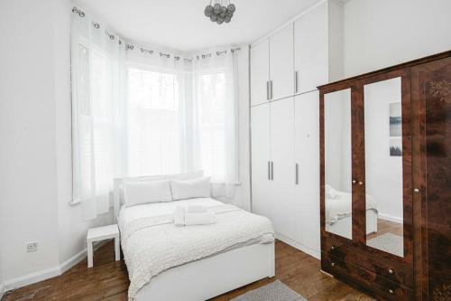 a white bedroom with a bed and a mirror at Super Stylish 1BD Flat with Garden in Leytonstone in London