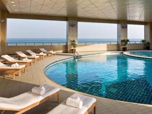 a pool in a hotel with lounge chairs and the ocean at Sofitel Al Khobar The Corniche in Al Khobar