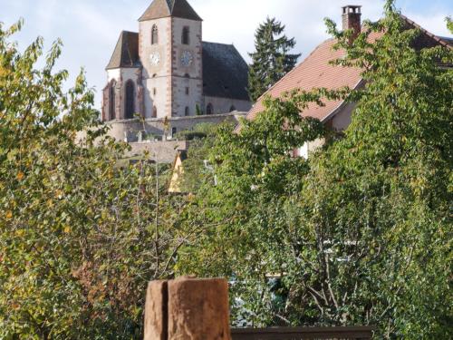 an old church with a clock tower behind trees at Charmant appartement rénové pour 4 pers avec terrasse à Hunawihr - FR-1-744-14 in Hunawihr