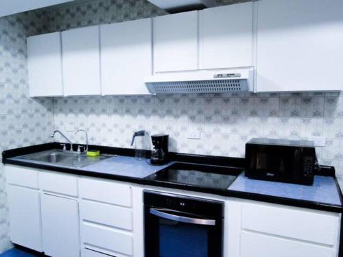 a kitchen with white cabinets and a sink and a microwave at Hermoso Apartamento Familiar in Caracas