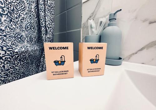 - deux boîtes assises sur un comptoir de salle de bains à côté d'un lavabo dans l'établissement NOUVEAU! Appartement Lille Moderne avec WiFi, TV, Proche Centre, à Lille