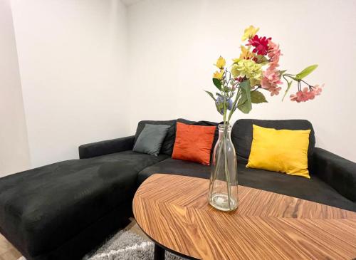 un canapé noir avec un vase de fleurs sur une table dans l'établissement L Eclat - Logement moderne proche Paris - Wifi, à Rueil-Malmaison