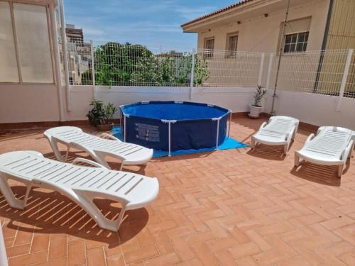 Casa con chimenea-4 habit.-2 baños-Gran terraza في ألكانار: فناء به ثلاثة كراسي بيضاء وحوض استحمام أزرق